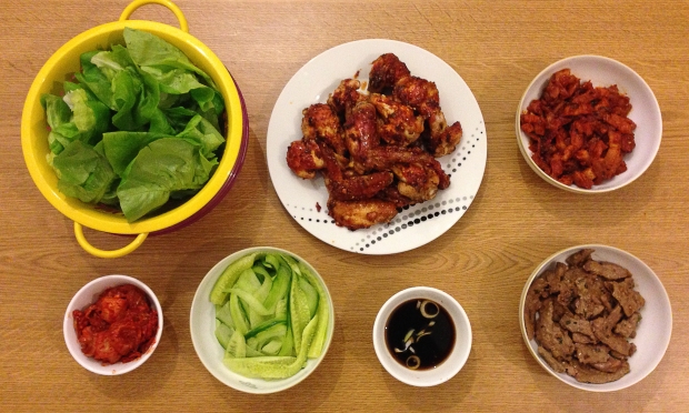 Top Left: Lettuce Top Middle: Korean Spicy Chicken Wings Top Right: Spicy Marinated Pork Bottom Far Left: Kimchi Bottom Left: Sliced Cucumber Bottom Right: Dipping Sauce Bottom Far Right: Bulgogi